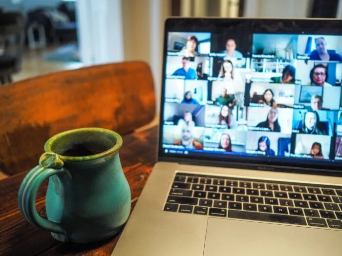 Laptop with a grid of remote meeting participants on screen next to a coffee mug on a table