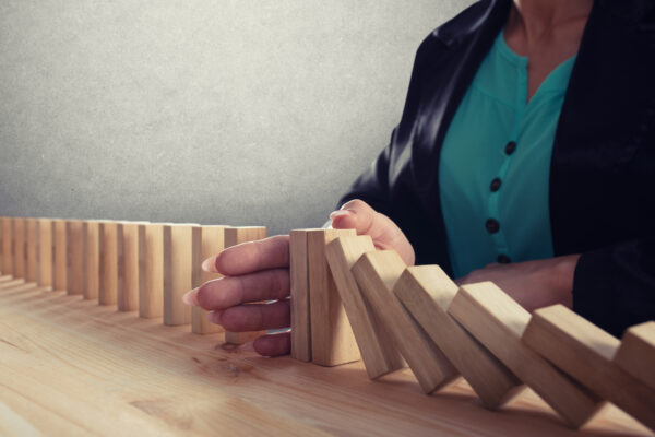 Woman's hand stops a row of wood dominos from falling.