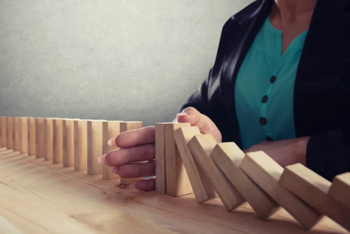 Woman's hand stops a row of wood dominos from falling.
