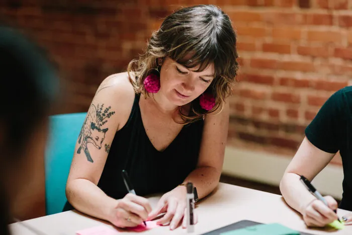 Lindsey wearing pink pom-pom earrings and writing on a pink Post-it