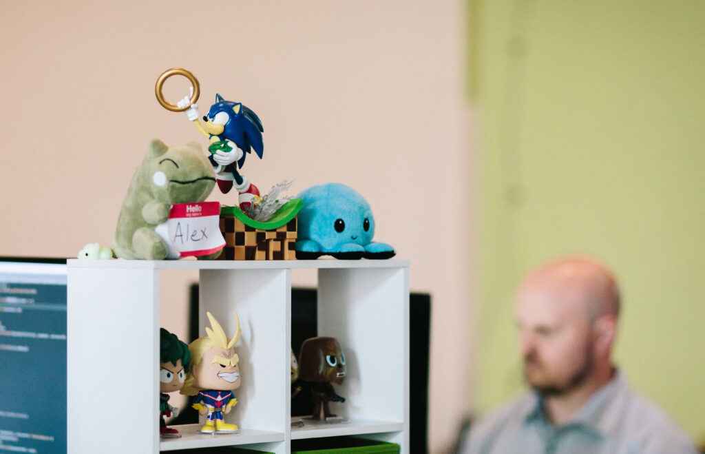 Sonic the Hedgehog figurine sits on top of a shelf while a developer codes in the background