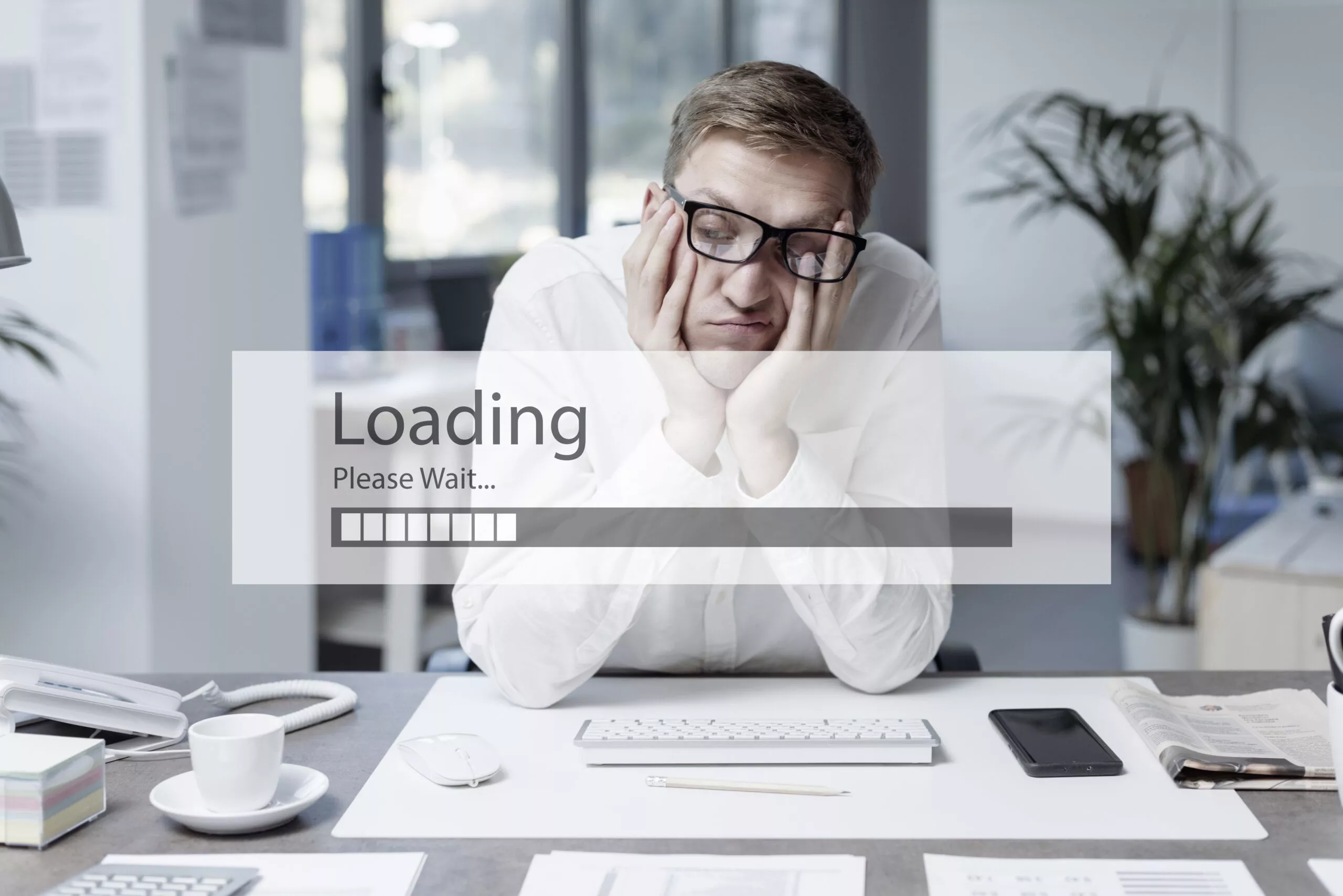 A man, frustrated and tired at a desk waiting for something to load