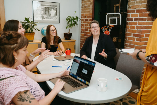 Team members at Pixo collaborating around a table, smiling and engaged in discussion during a project planning meeting.