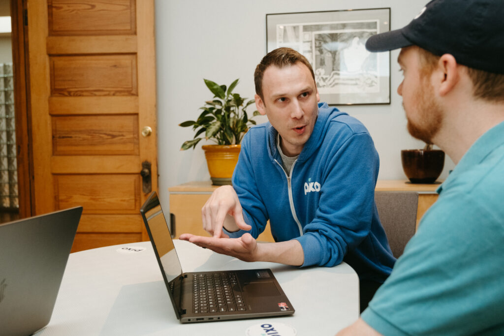 Jeremy Boehme and Matt Fotzler talking to one another at a desk with open laptops