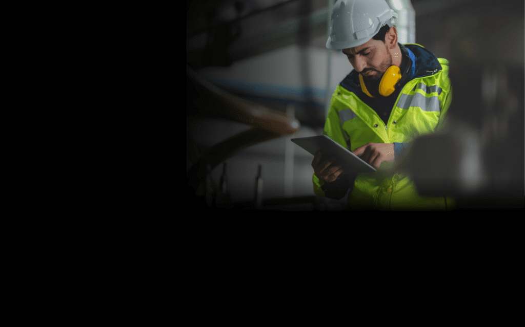 man in yellow jacket and white hard hat using a tablet in an industrial setting