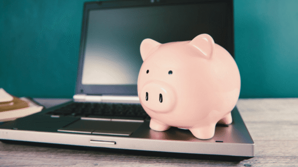 pink piggy bank sitting on the keyboard of an open laptop computer