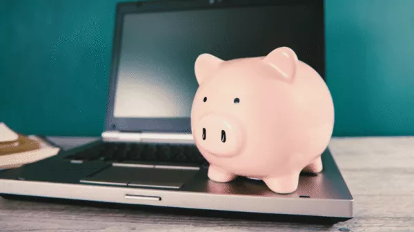 pink piggy bank sitting on the keyboard of an open laptop computer